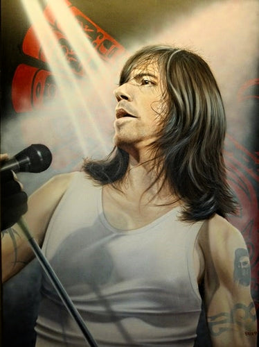 Anthony Kiedes is shown in a white tank top, picturing his tattooed arms. He is looking towards the left, slightly angled towards a microphone on a stand. Strobe lights flash in the background, covering the black and red background.