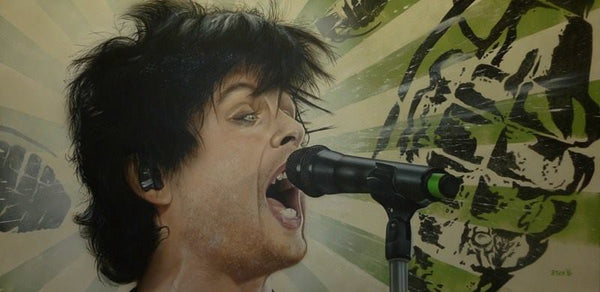 Billie Joel Armstrong of Green Day is pictured from the neck up, expressively singing into a microphone on a stand. A green and white striped background is printed with several black grenades.