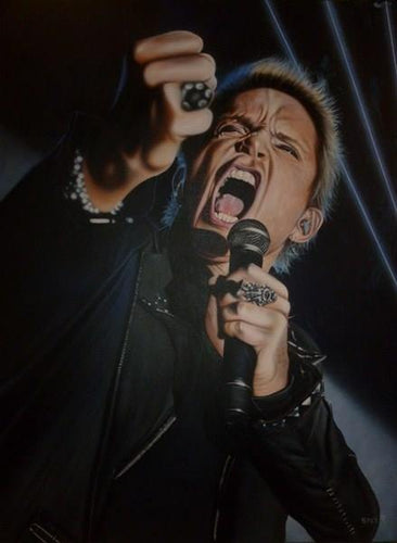 Billy Idol is shown from the waist up from a lower angle. He is wearing all black and has multiple rings and other articles of silver jewelry. His face is scrunched as he is yelling into a microphone in his hand. There is a black background with some thin white lights shining across it.