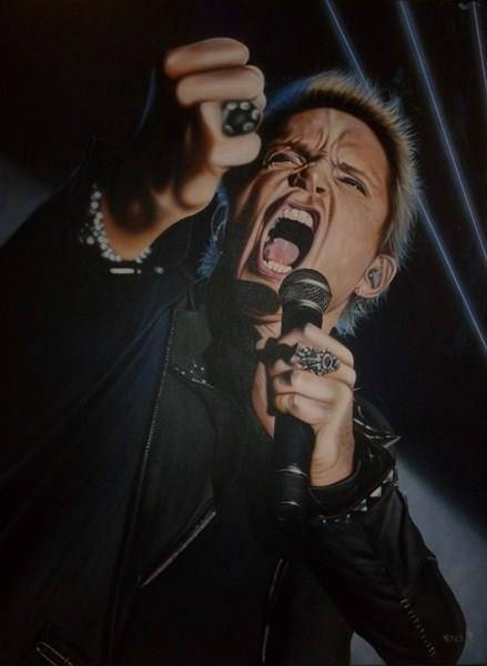 Billy Idol is shown from the waist up from a lower angle. He is wearing all black and has multiple rings and other articles of silver jewelry. His face is scrunched as he is yelling into a microphone in his hand. There is a black background with some thin white lights shining across it. 
